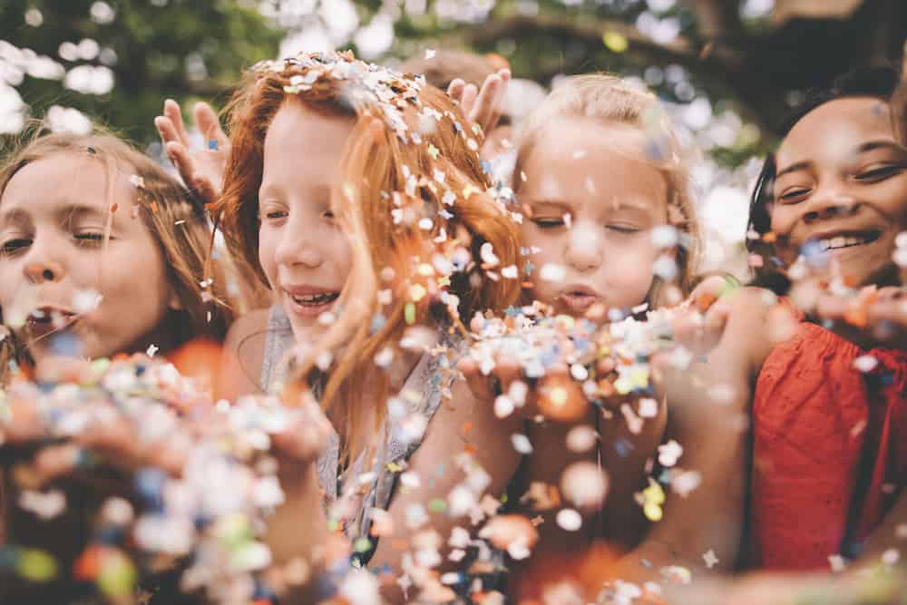Colourful paper confetti being blown at the camera by children